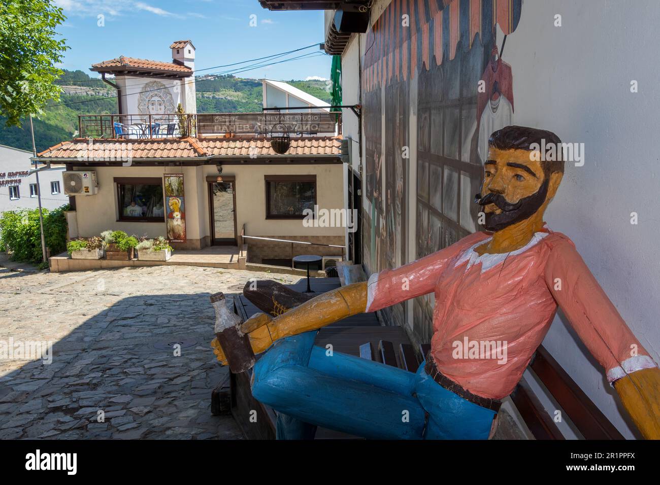 Sculpture en bois grandeur nature d'un homme du coin assis sur un banc de rue et buvant une bière, dans une rue de Veliko Tarnovo, Bulgarie. Banque D'Images