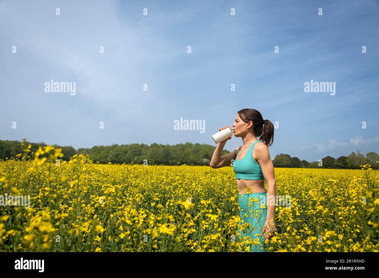 femme sportive buvant de l'eau après avoir coué dans un champ jaune Banque D'Images