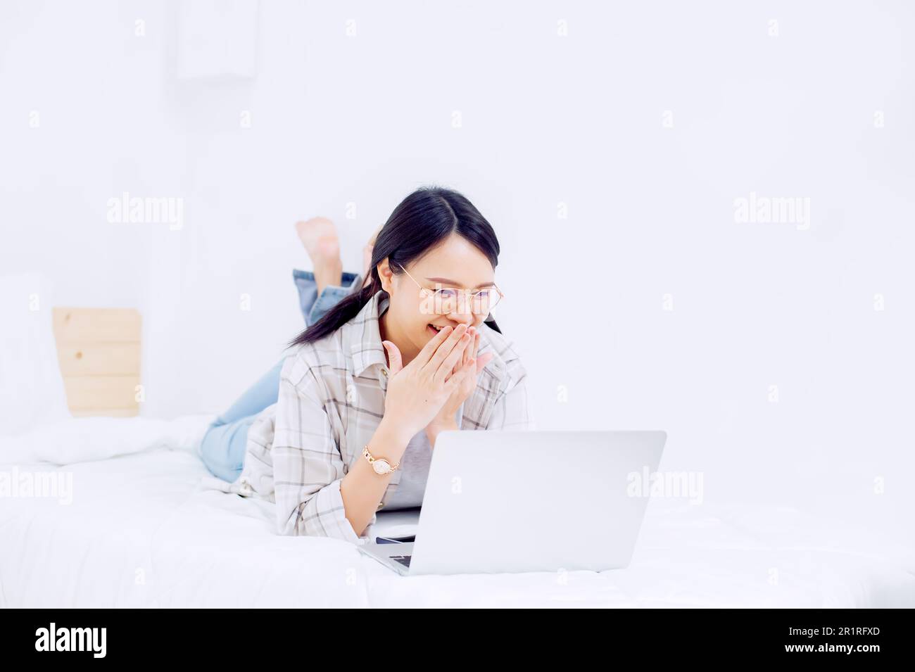 Femme souriante couchée sur son lit, effectuant un appel vidéo sur son ordinateur portable Banque D'Images