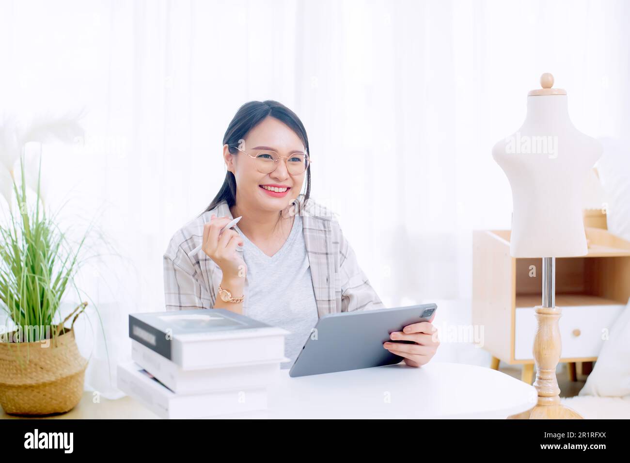 Femme souriante de mode assis à une table travaillant sur une tablette numérique Banque D'Images
