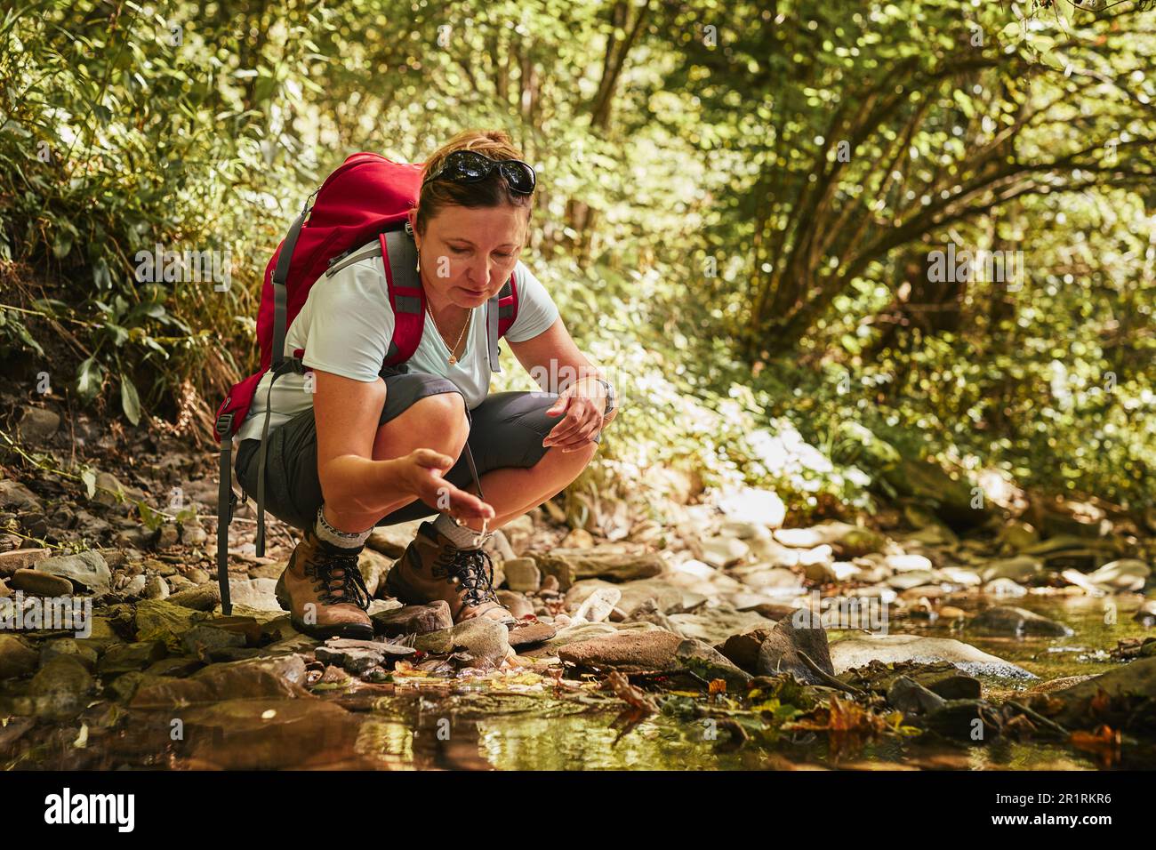 Voyage de randonnée avec le concept de sac à dos image. Backpacker femelle dans trekking bottes traversant la rivière de montagne. Femme randonnée dans les montagnes pendant l'été t Banque D'Images