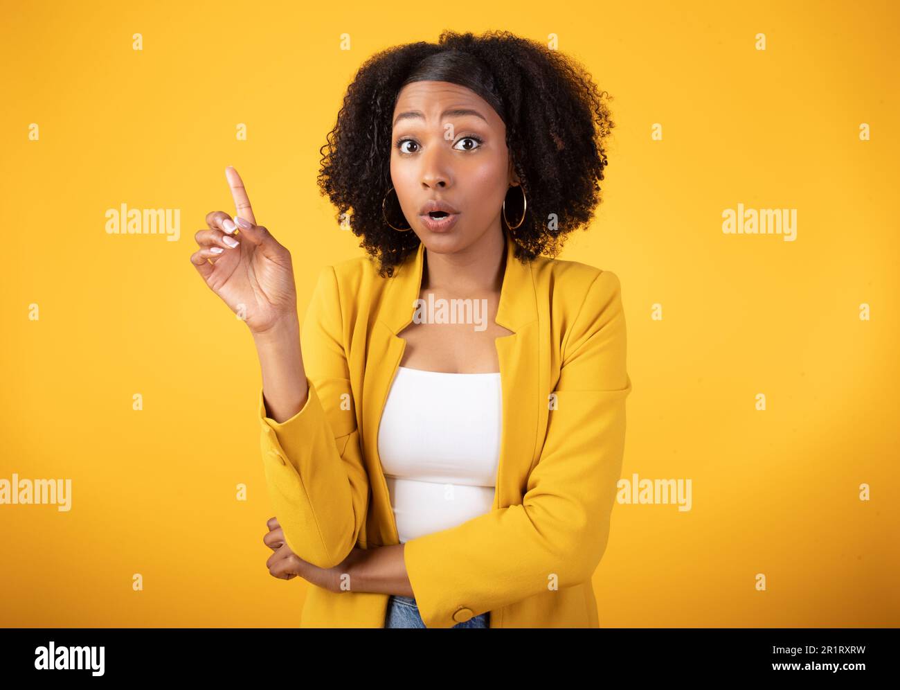 Moment Eureka. Une femme noire émotive qui pointe le doigt vers le haut et s'exclame, regardant l'appareil photo sur fond jaune Banque D'Images