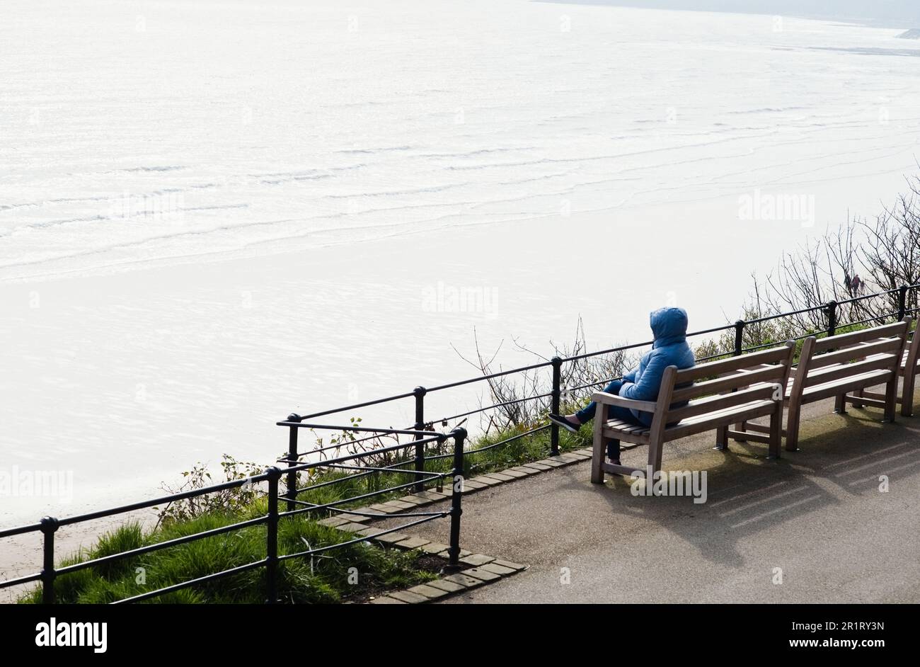 Une femme seule à capuchon qui profite du soleil d'hiver et surplombe la baie sud de Scarborough Banque D'Images