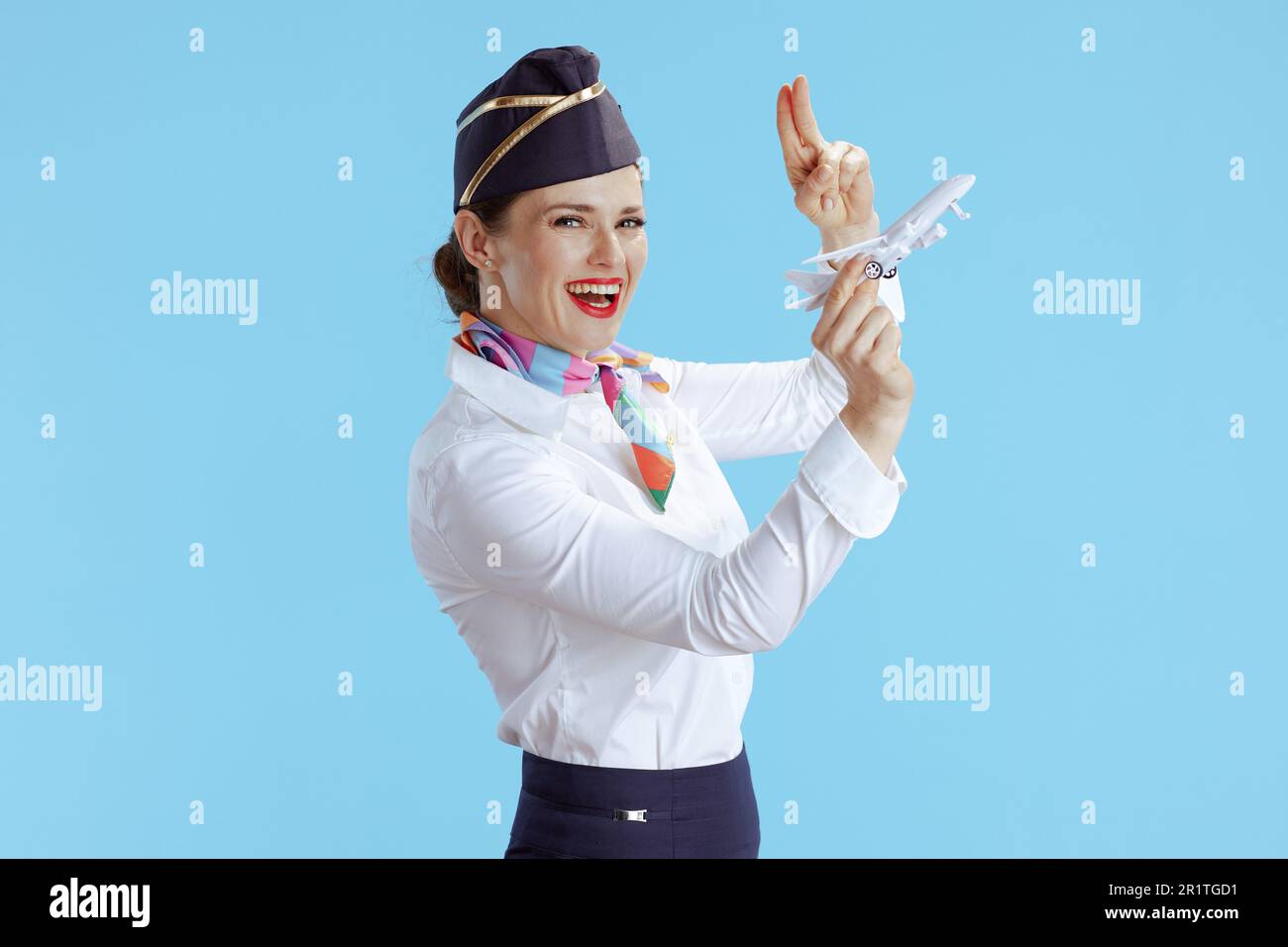 bonne femme élégante de gardien de vol sur fond bleu en uniforme avec un petit salute d'avion. Banque D'Images