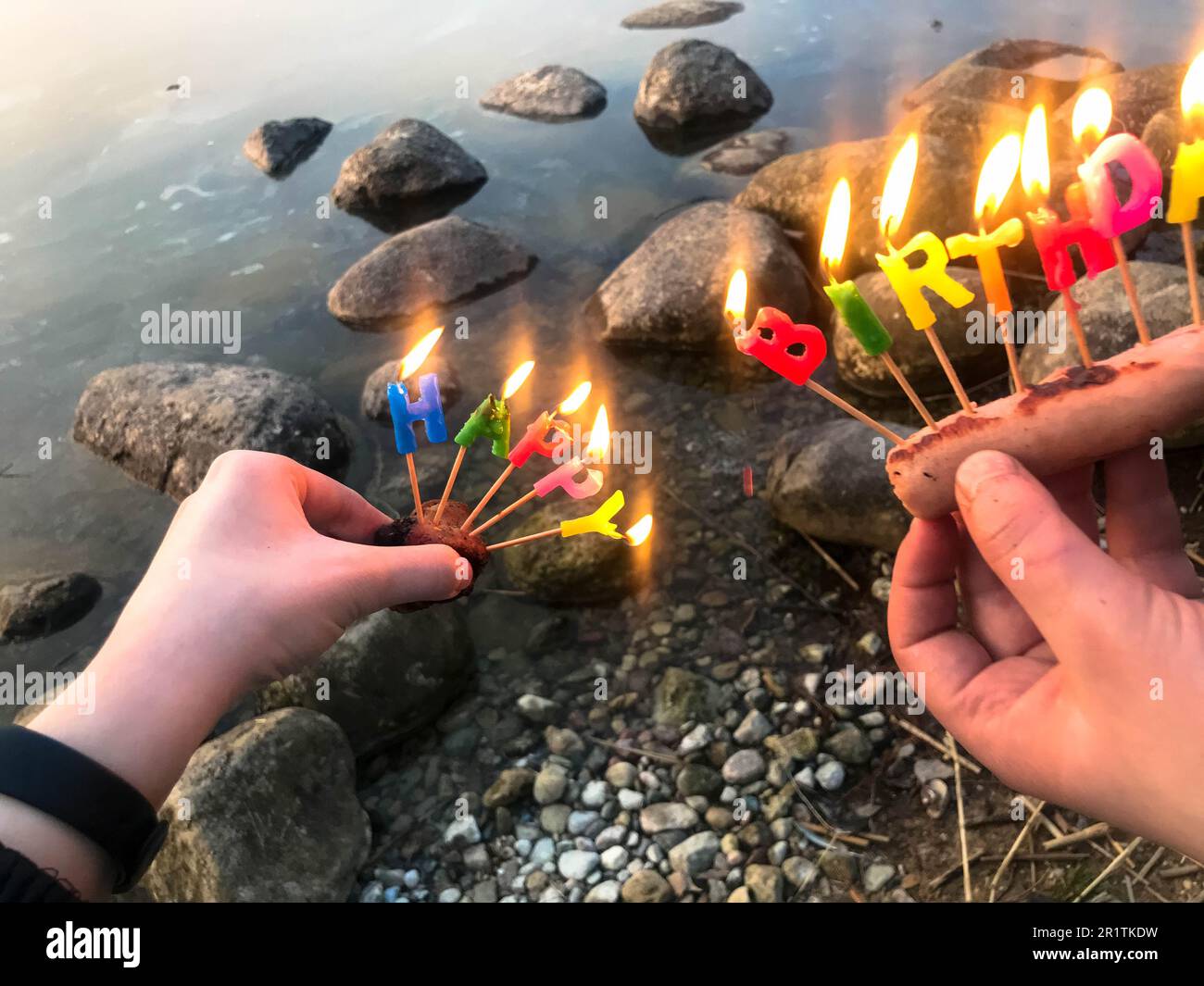 Inscription d'anniversaire brûlante faite de bougies de vacances dans les mains d'un homme et d'une femme face à l'eau du lac de l'océan. Concept: birt Banque D'Images