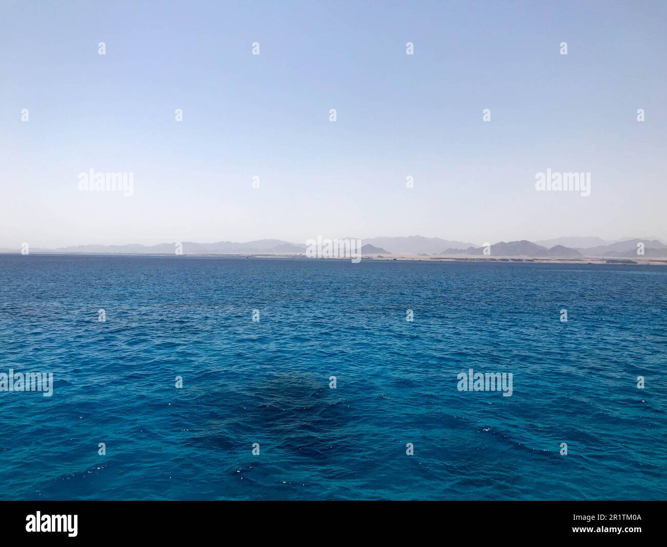 Paysage de bleu transparent perlant eau salée de mer, mer, océan avec vagues, ondules sous le soleil brûlant sur la toile de fond de la montagne lointaine Banque D'Images