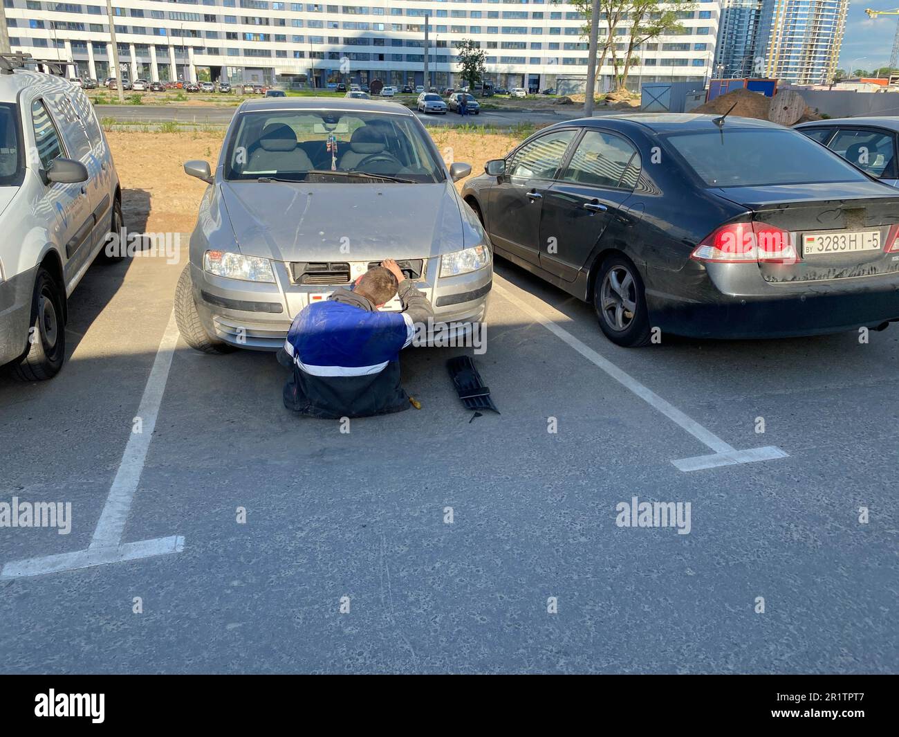 Un serrurier de sexe masculin répare une voiture qui se trouve sous le capot dans un parking. Réparation automobile à faire soi-même. Banque D'Images