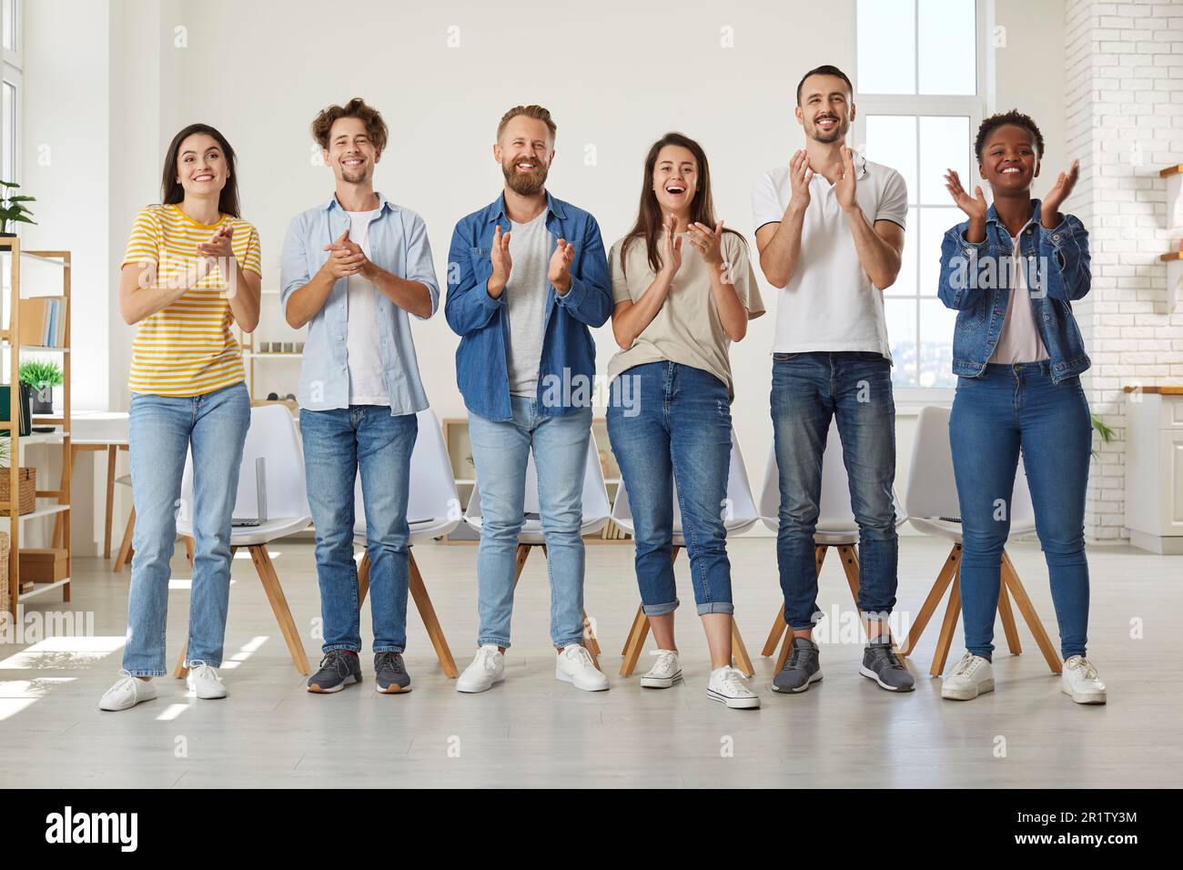 Les personnes amicales multiraciales dans des vêtements décontractés se tiennent à la ligne et applaudissent à vous regarder. Banque D'Images