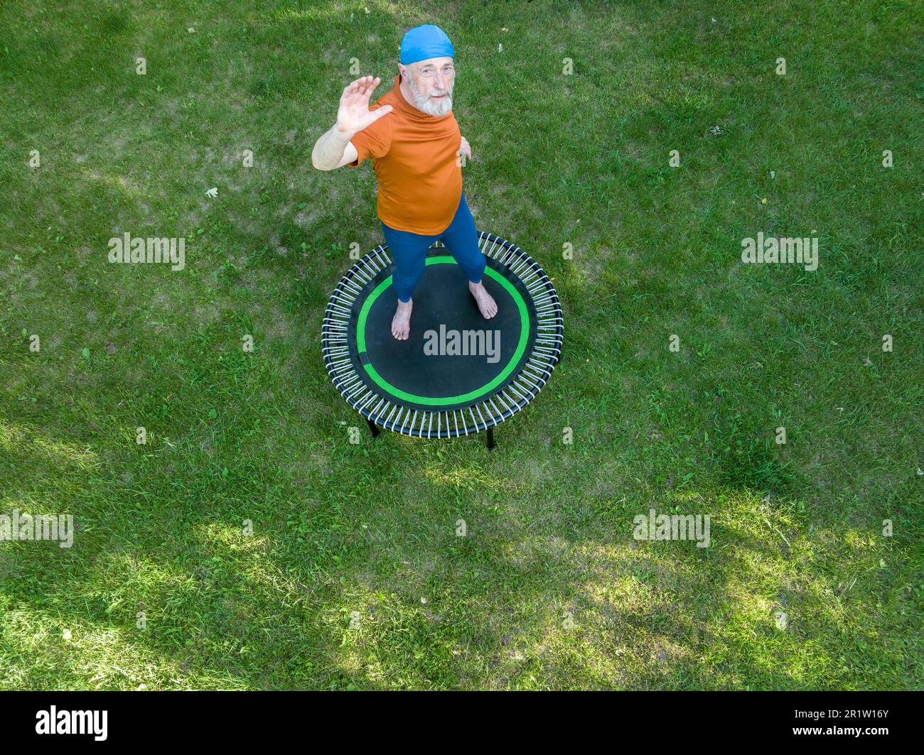 senior surpoids homme s'exerçant sur un mini trampoline dans son arrière-cour, fitness et rebondissement concept, vue aérienne Banque D'Images