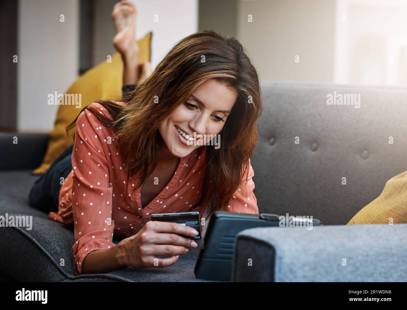 Confort et commodité, crédit offert. une jeune femme attrayante utilisant une tablette numérique et une carte de crédit sur le canapé à la maison. Banque D'Images