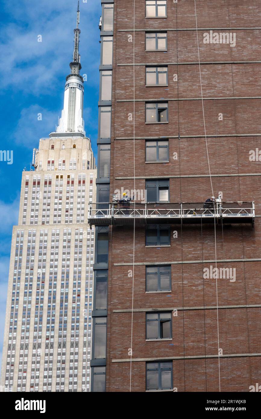 Les travailleurs effectuent un repointage de briques sur une plate-forme suspendue avec l'Empire State Building en arrière-plan, 2023, New York City, États-Unis Banque D'Images