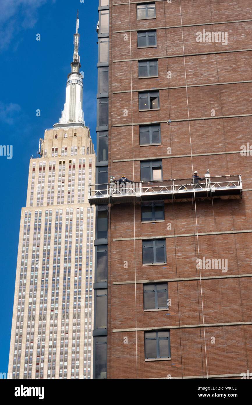 Les travailleurs effectuent un repointage de briques sur une plate-forme suspendue avec l'Empire State Building en arrière-plan, 2023, New York City, États-Unis Banque D'Images