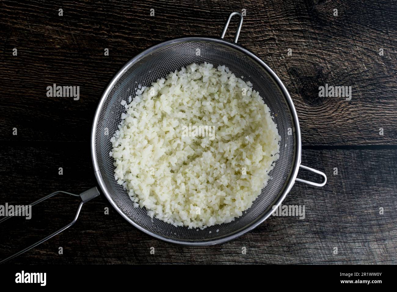 Riz au chou-fleur congelé décongelé dans un tamis en maille: Chou-fleur de riz dans une passoire placée sur un bol à mélanger Banque D'Images