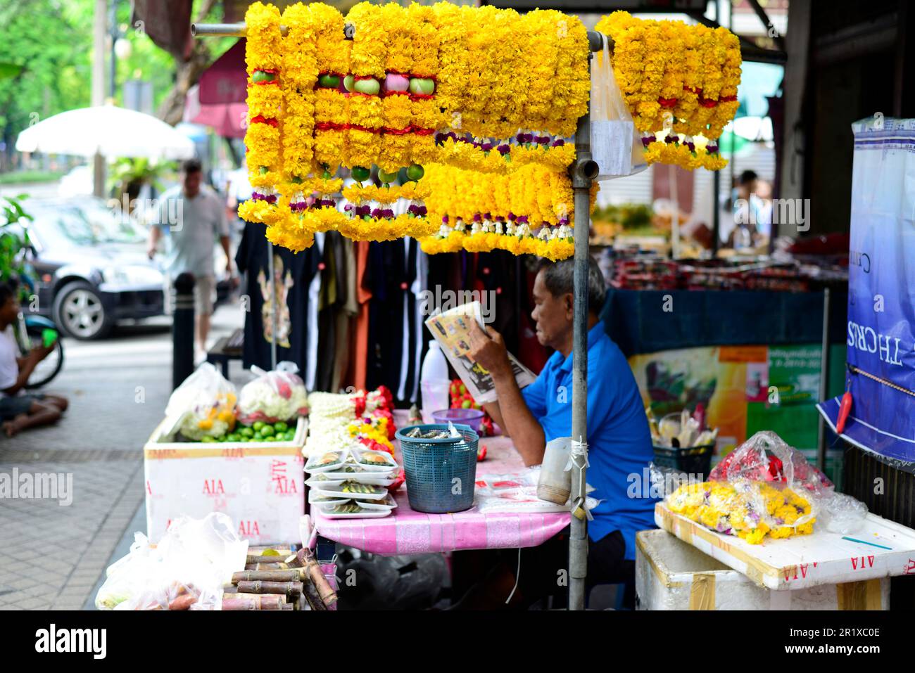 Un vendeur de guirlande de fleurs lisant le journal du matin. Bangkok, Thaïlande. Banque D'Images