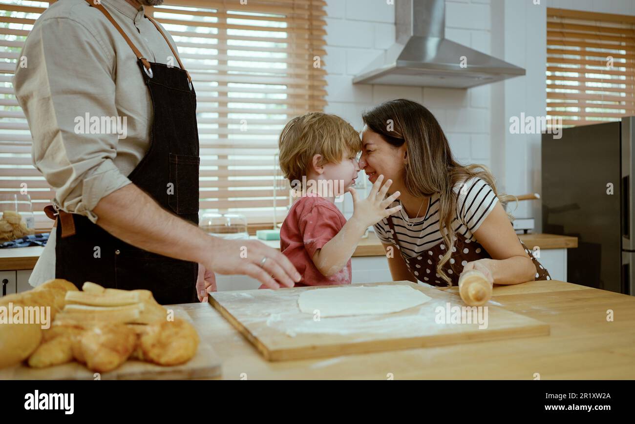 Le père et la mère enseignent à bébé le pétrissage de la pâte sur le comptoir de cuisine à la maison. Les parents et le garçon gamin apprécient et s'amusent à cuisiner à l'intérieur ensemble. Banque D'Images