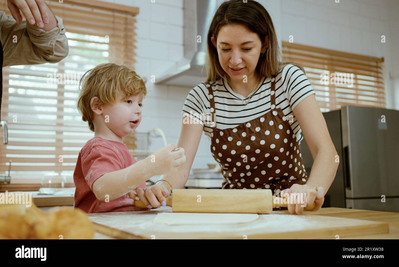 Le père et la mère enseignent à bébé le pétrissage de la pâte sur le comptoir de cuisine à la maison. Les parents et le garçon gamin apprécient et s'amusent à cuisiner à l'intérieur ensemble. Banque D'Images