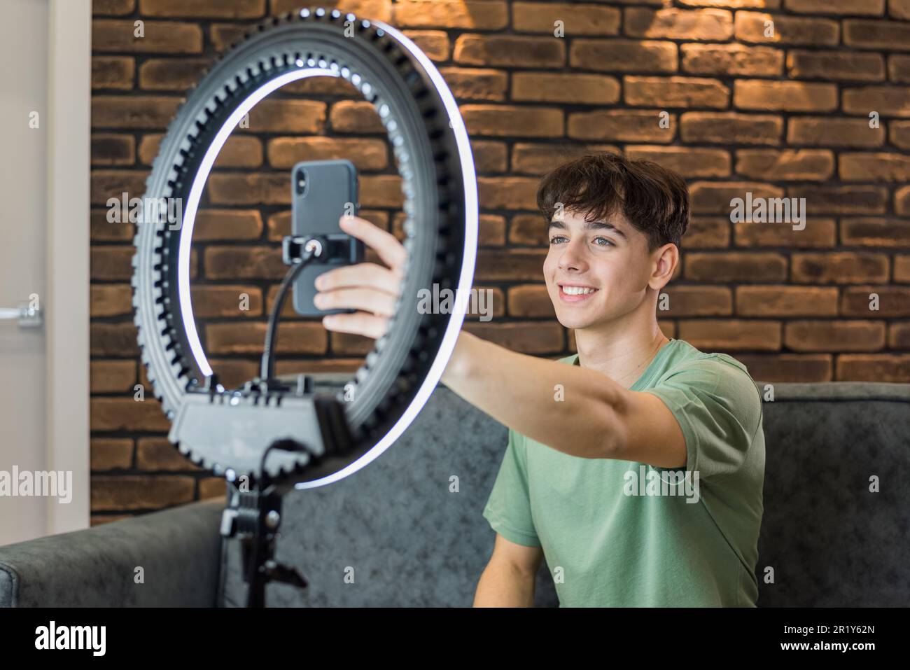 Un jeune homme souriant blogueur influenceur se prenant sur un smartphone sur un trépied avec anneau lumineux dans un studio Banque D'Images