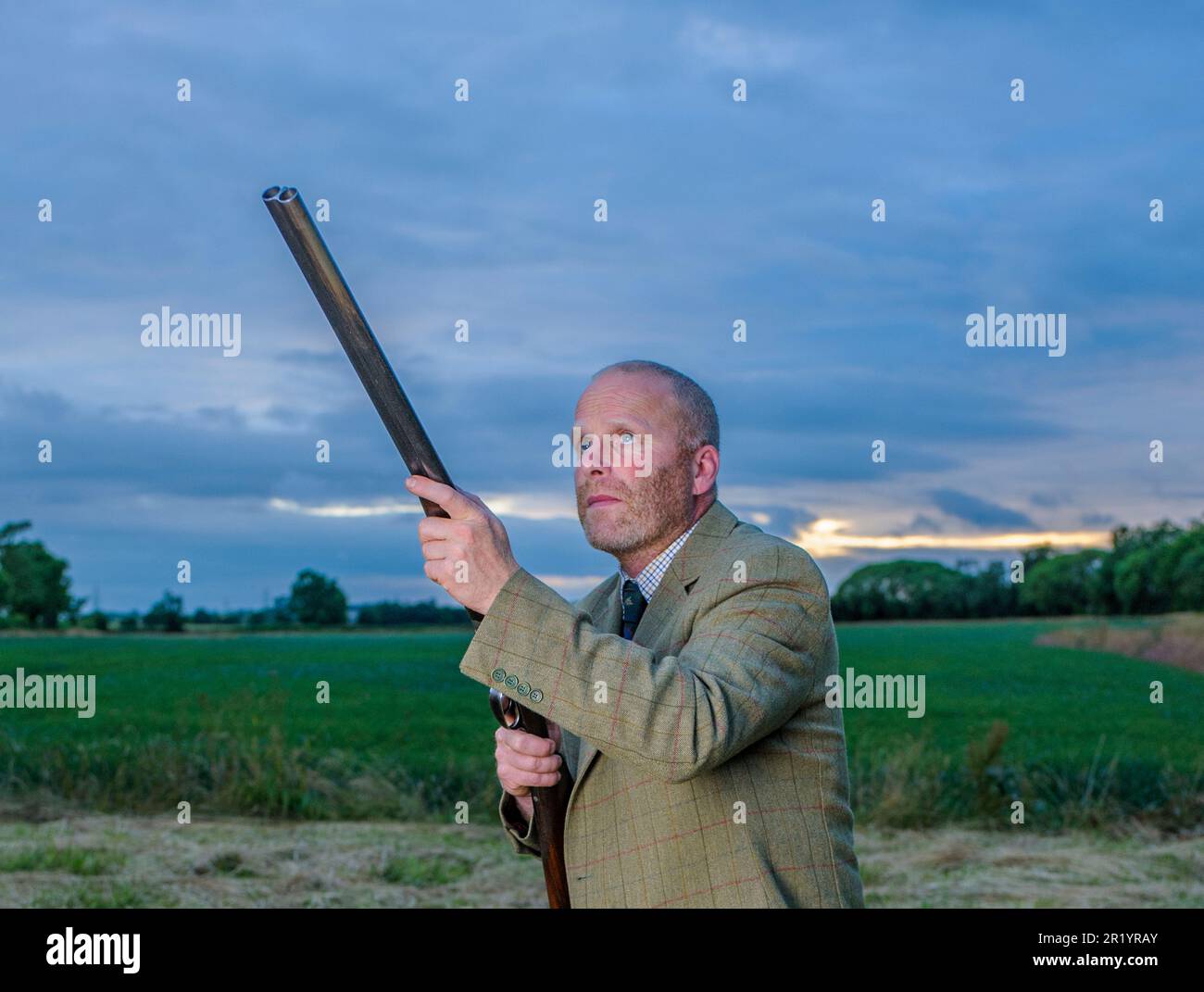 Un homme anglais se tenait au crépuscule dans un costume de tir en tweed avec un fusil de chasse Banque D'Images