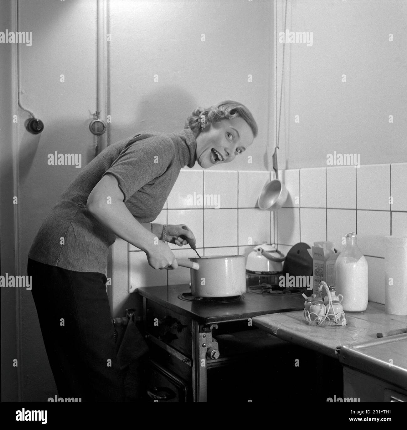 Dans la cuisine 1950s. Intérieur d'une cuisine et une jeune femme debout à la cuisinière de cuisine faisant un visage drôle tout en cuisinant quelque chose dans une casserole. Elle est actrice Maj-Britt Thörn, 1923-2023. Suède 1951 Conard réf. 1652 Banque D'Images
