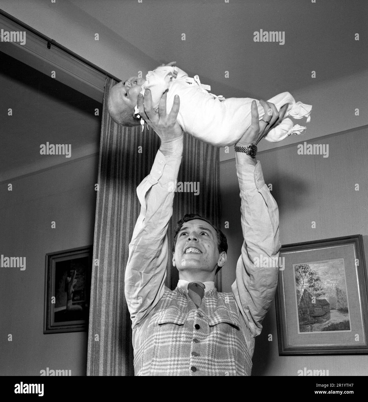Homme du 1950s. Le danseur suédois Mario Mengarelli lors d'une séance photo à domicile avec son nouveau-né qu'il tient dans les mains au-dessus de sa tête. Suède 1952 réf. 1958 Banque D'Images