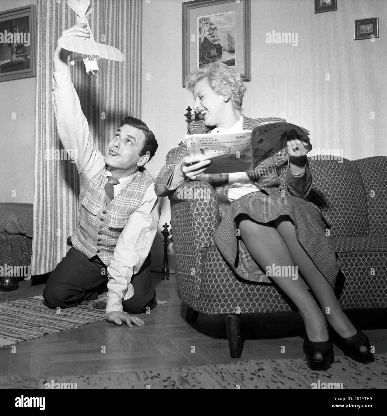 Dans le 1950s. Un jeune couple dans leur appartement où il est photographié jouant avec un avion modèle. Elle est assise dans le canapé avec un magazine et rit à lui. Il danse Mario Mengarelli 1925-2002 dans une séance photo à domicile. Suède 1952. Conard réf. 1958 Banque D'Images