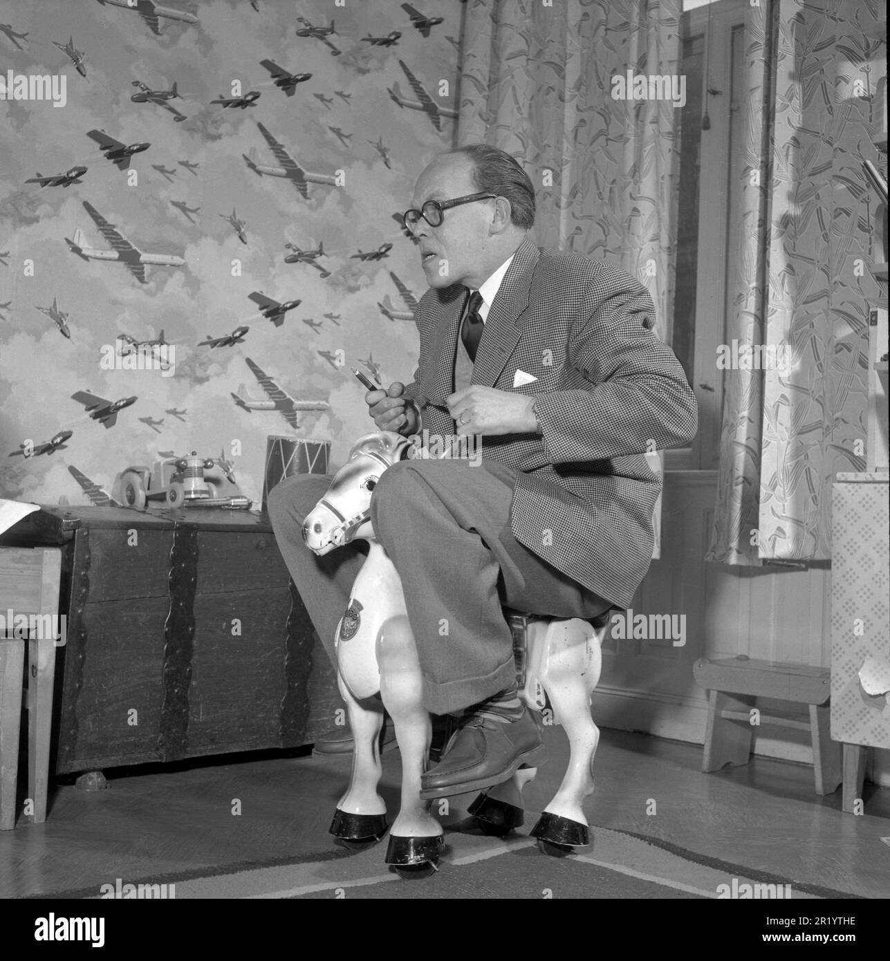 Amusez-vous dans le 1950s. Un homme joue seul sur un cheval jouet pour enfants. Il est écrivain et journaliste Olle Carle, 1909-1998. Suède 1953. Conard réf. 2376 Banque D'Images