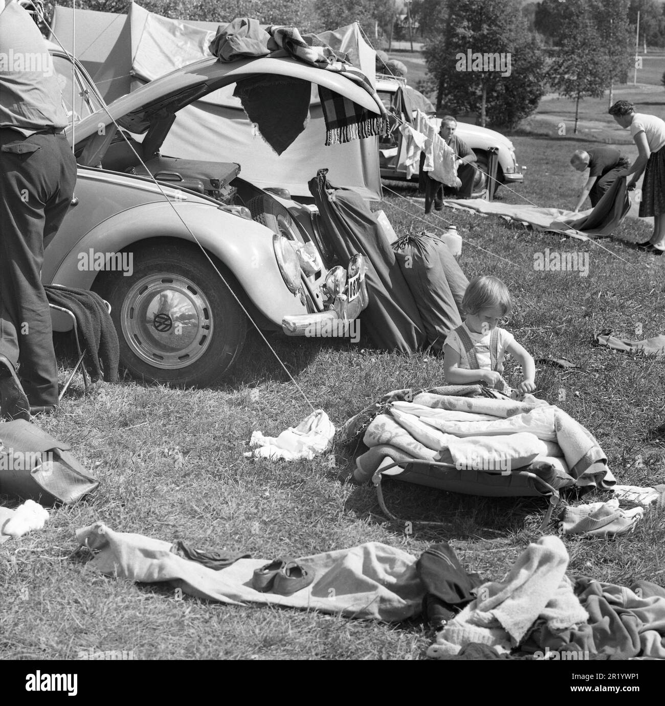 Camping dans le 1960s. Un camping où les familles passent des parties de leurs vacances d'été. Leurs voitures sont vues en arrière-plan avec le matériel de camping transporté sur le porte-bagages de toit. Värmland Suède 1962. Réf. BV99-2 Banque D'Images
