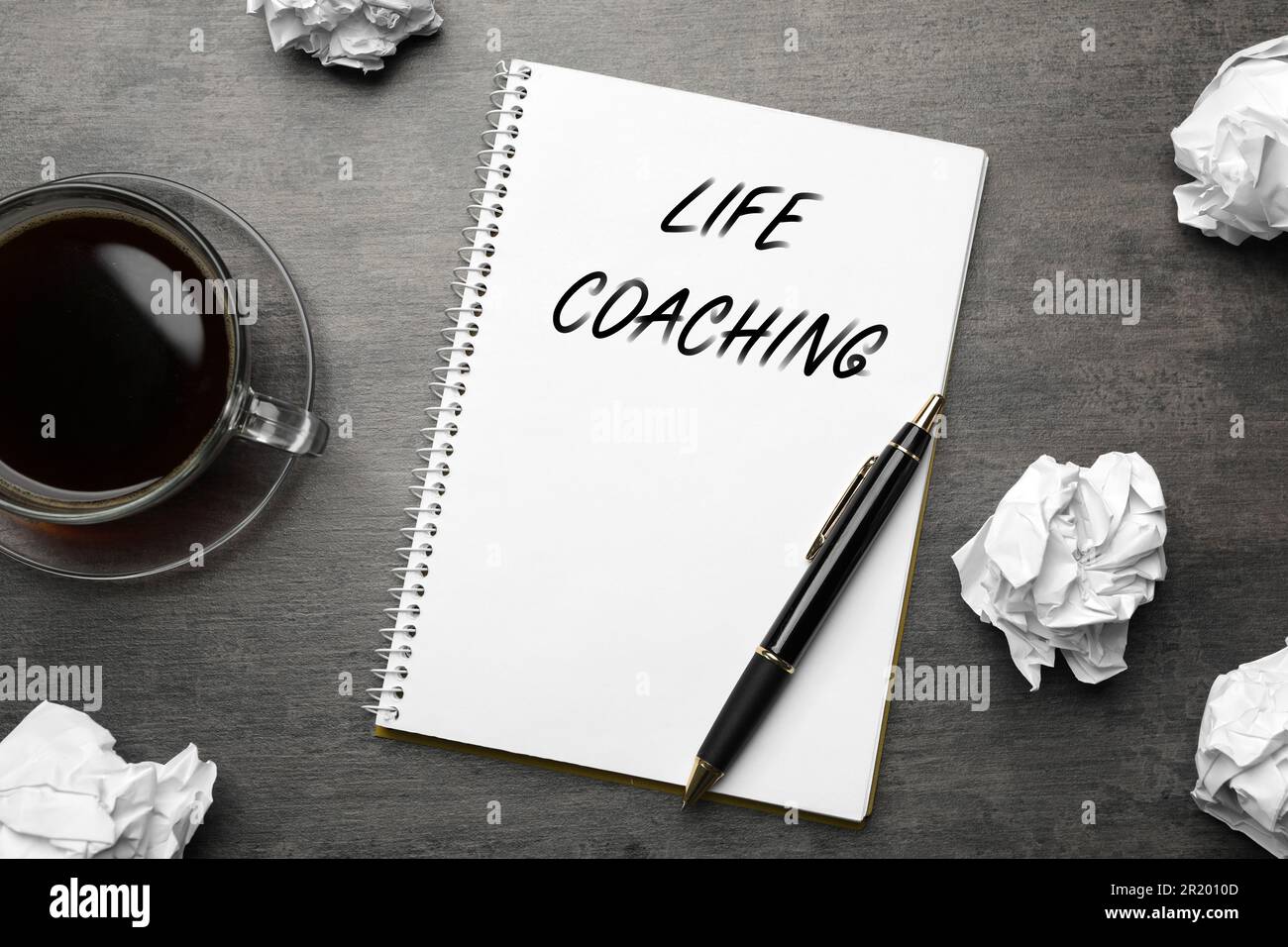 Phrase Life Coaching écrit dans un cahier, une tasse de café, papier froissé et stylo sur une table grise, plat Banque D'Images