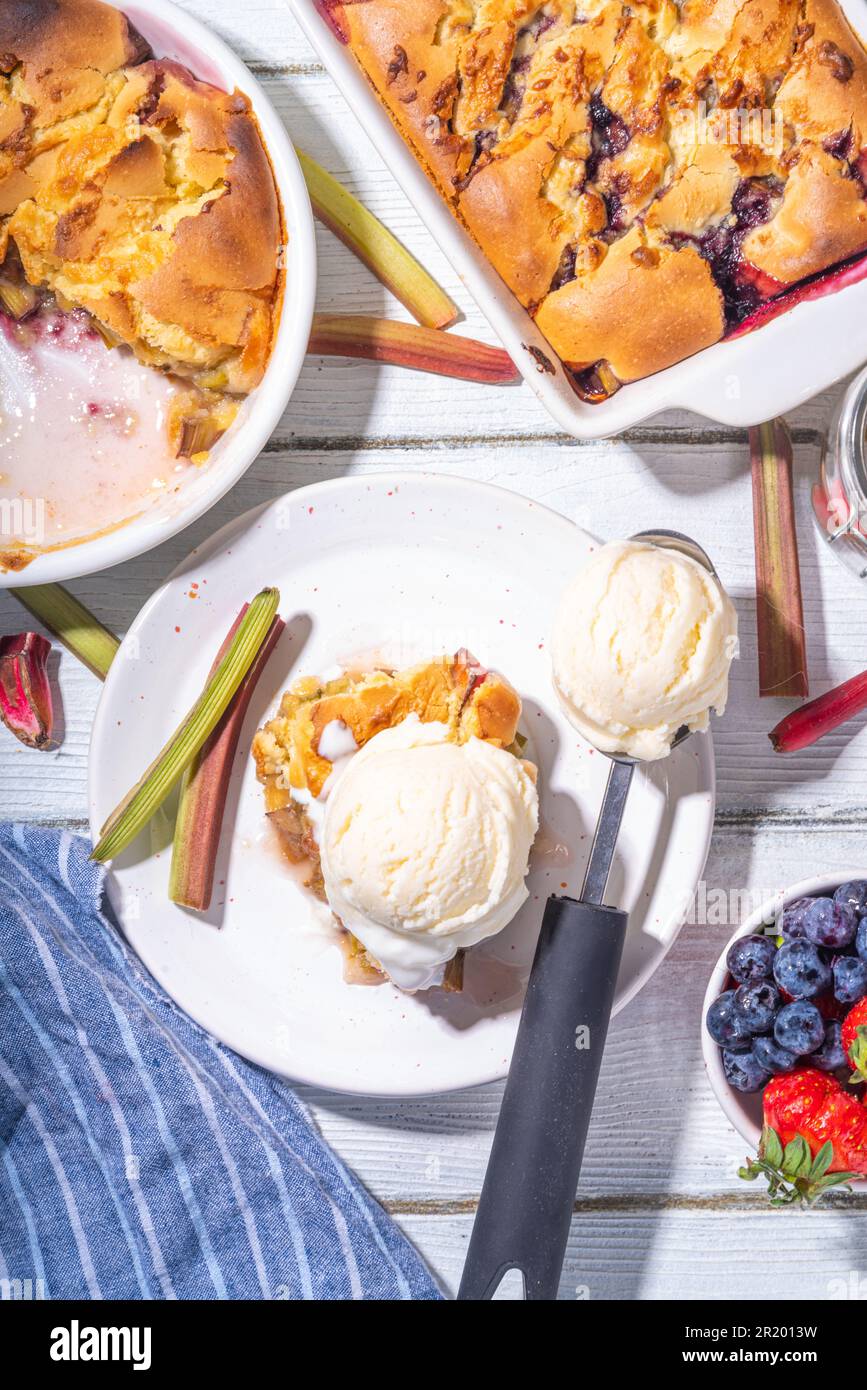 Tarte parée à la framboise aux baies, gâteau maison à l'éponge avec rhubarbe sucrée et fraise, servi avec boule de glace à la vanille, sur un k en bois blanc ensoleillé Banque D'Images