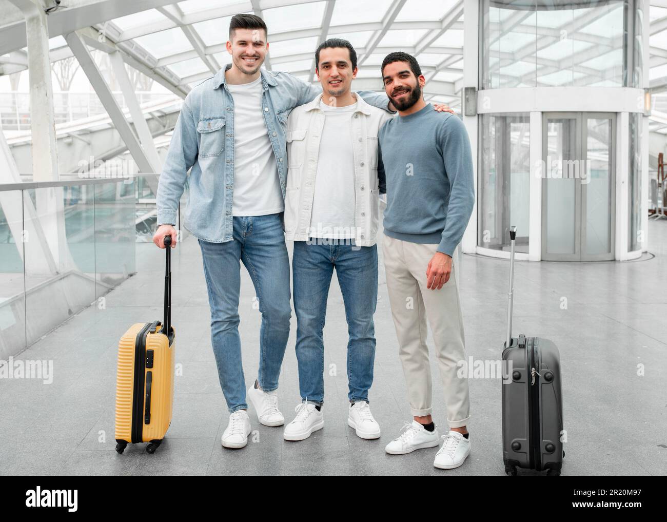 Trois passagers hommes qui s'embrasent en posant avec des bagages dans l'aéroport moderne Banque D'Images