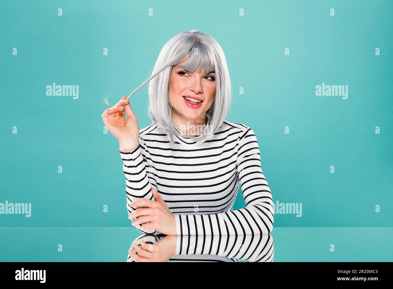 Portrait de la jeune femme positive dans une tenue tendance souriant et regardant loin tout en étant assis sur fond turquoise Banque D'Images