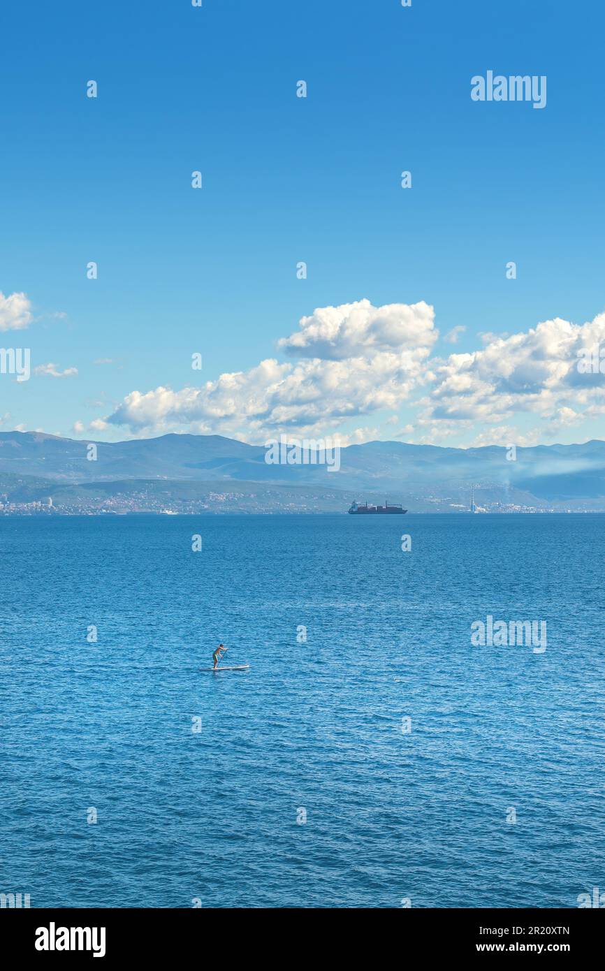 Personne méconnaissable paddle-board debout sur la mer Adriatique du golfe de Kvarner vue de la côte de la ville de Lovran, attention sélective Banque D'Images