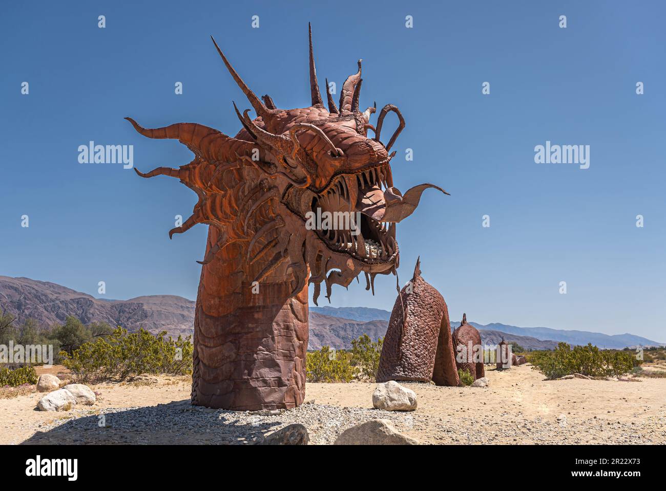 Borrego Springs, CA, Etats-Unis - 24 avril 2023 : statue de dinosaure de serpent géant préhistorique en métal rouillé brun, d'avant en arrière, sur un désert sablonneux sous ciel bleu, Banque D'Images