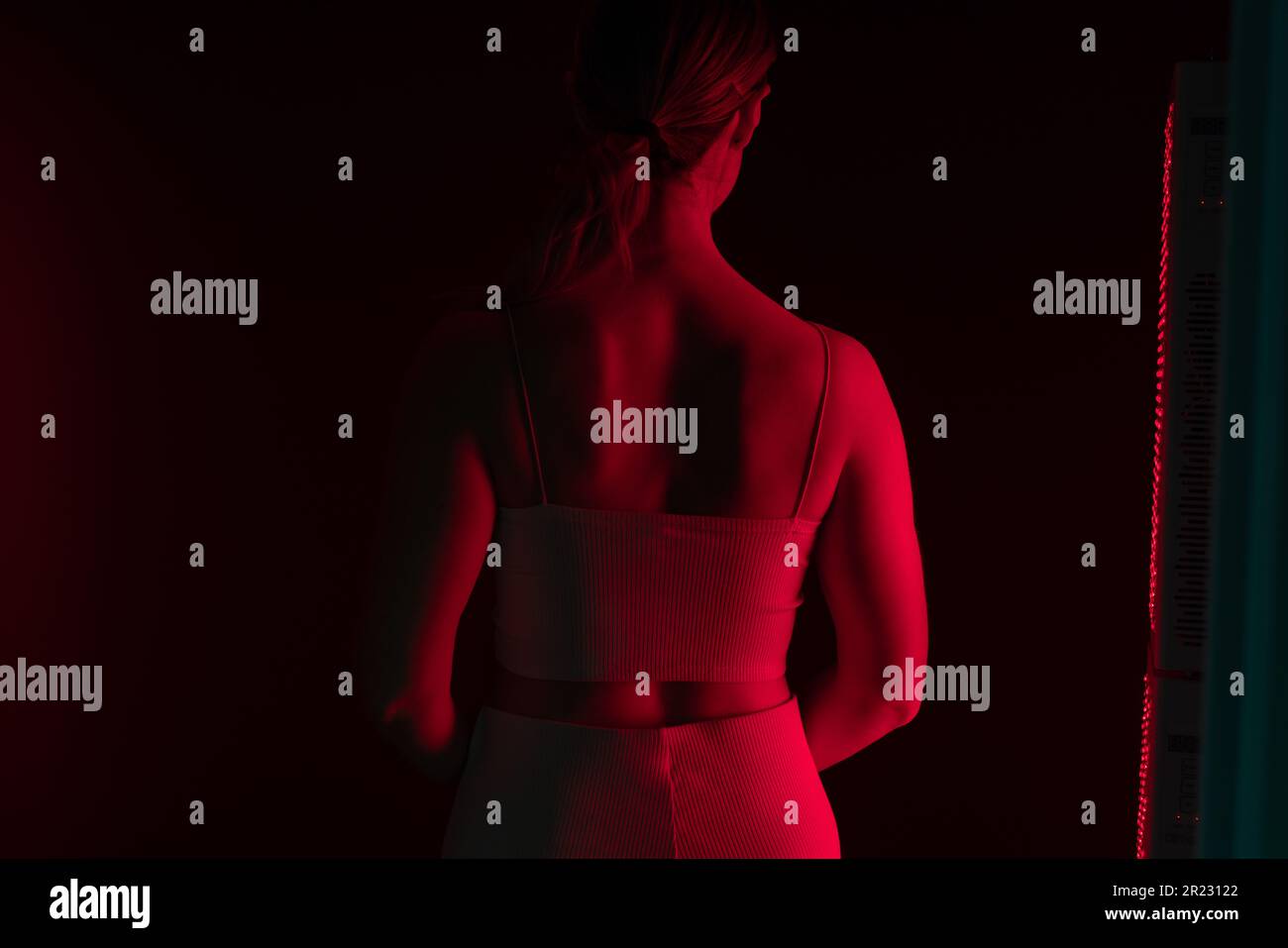 Vue arrière d'une femme recevant une luminothérapie à la lumière rouge sur son dos. Femme debout à côté d'un appareil de lumière rouge dans un spa cosmétique. Traiteurs anti-âge pour les soins de la peau Banque D'Images