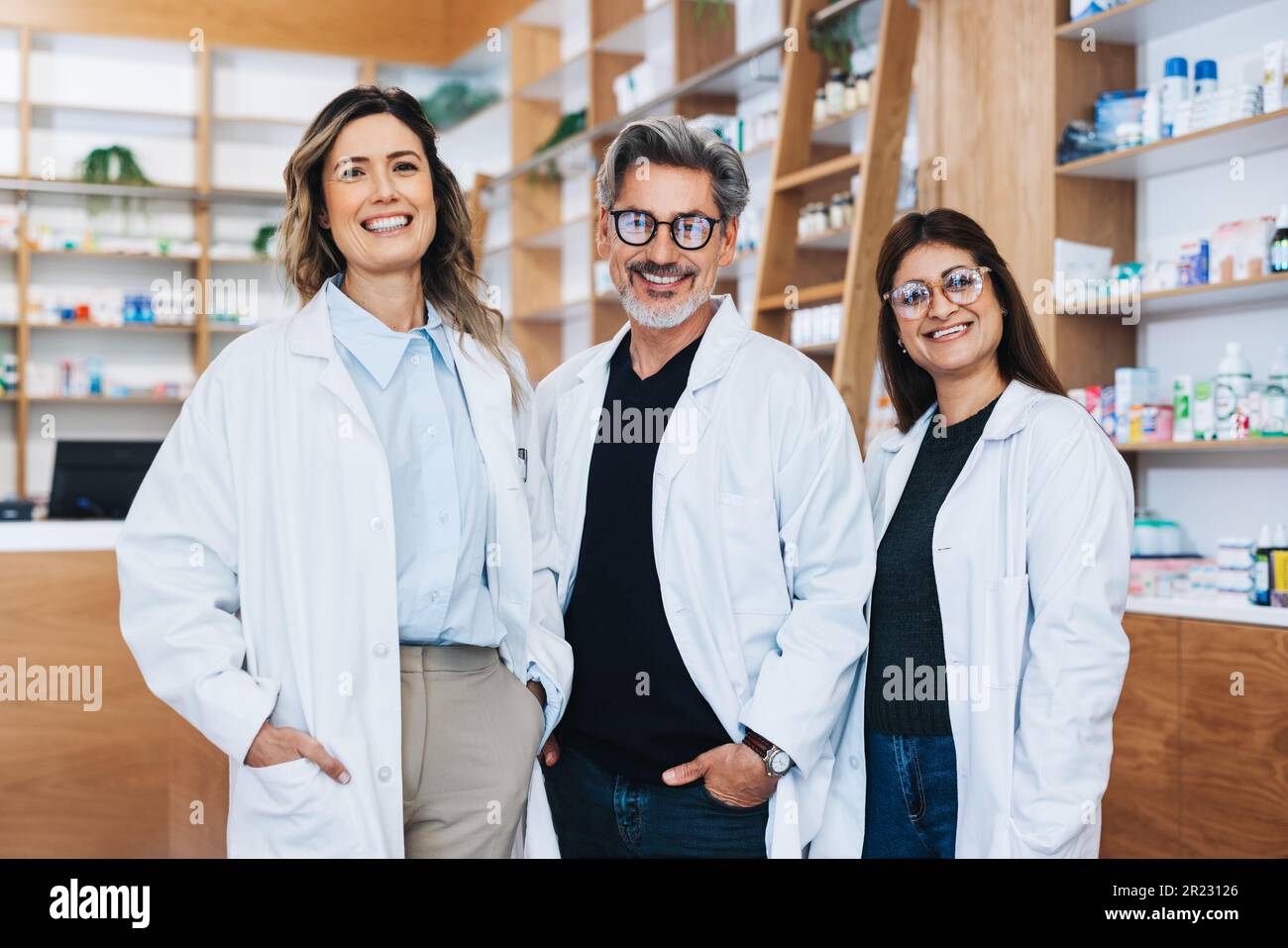 Groupe de pharmaciens debout ensemble et regardant l'appareil photo dans un chimiste. Trois fournisseurs de soins de santé travaillant dans une pharmacie. Banque D'Images