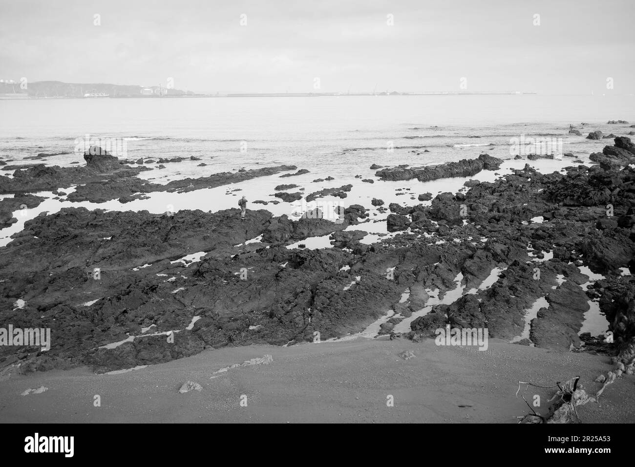 Figure éloignée d'un homme marchant sur les rochers à marée basse à la plage de Rinconin, ou plage de Cervigon, à Gijon, en Espagne. Banque D'Images