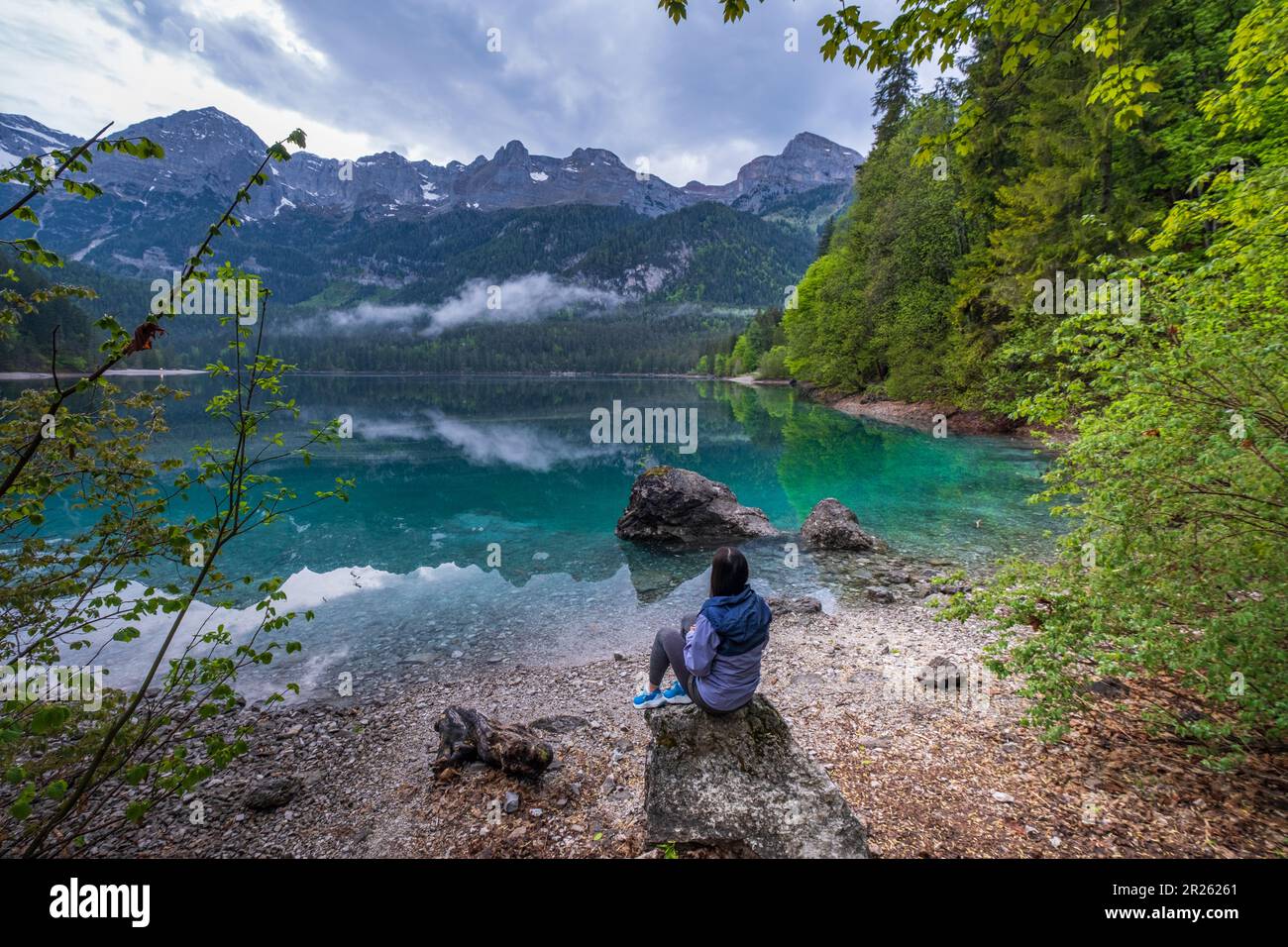 Jeune femme assise au bord de la mer et bénéficiant de la vue sur le majestueux lac Tovel, dans le nord de l'Italie. Dolemites, Alpes italiennes. Voyages en Europe. Banque D'Images