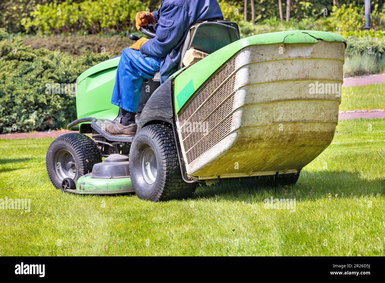 Un travailleur en combinaison bleue conduit une tondeuse à gazon et tond  l'herbe verte de la pelouse. sur un fond flou d'un jardin de printemps.  Copier l'espace Photo Stock - Alamy