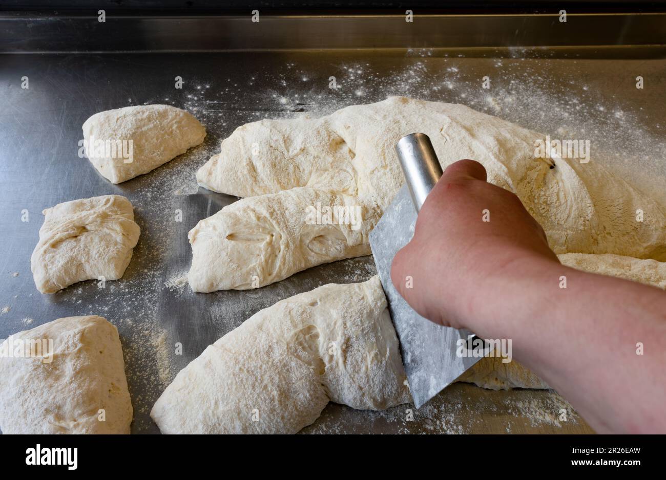 Chef coupant de la pâte Ciabatta sur une table en métal en utilisant un banc de grattage vue latérale Banque D'Images