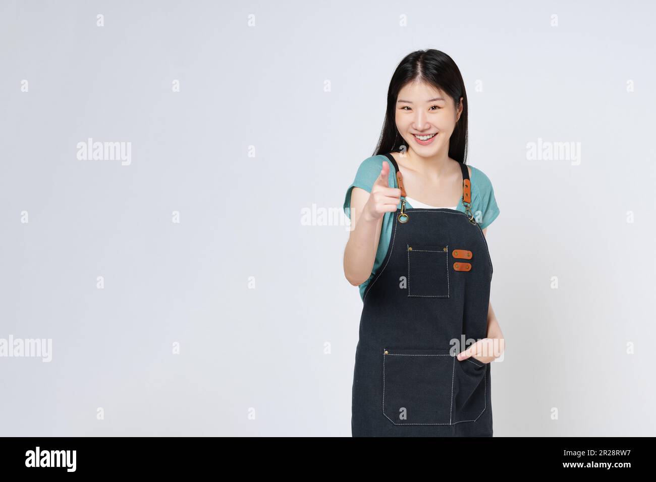 Jeune femme chef ou serveur souriant et pointant vers l'avant, regardant l'appareil photo isolé sur fond blanc. Banque D'Images
