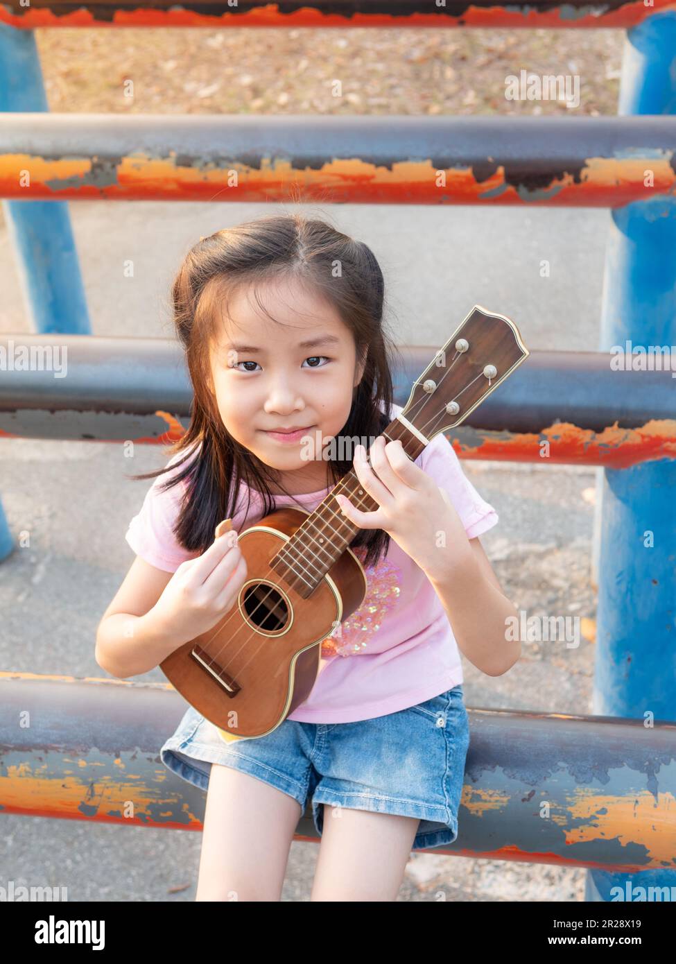 Petite fille asiatique jouer l'ukulele, dans le jardin sur le tuyau en acier, pratiquer à jouer Banque D'Images