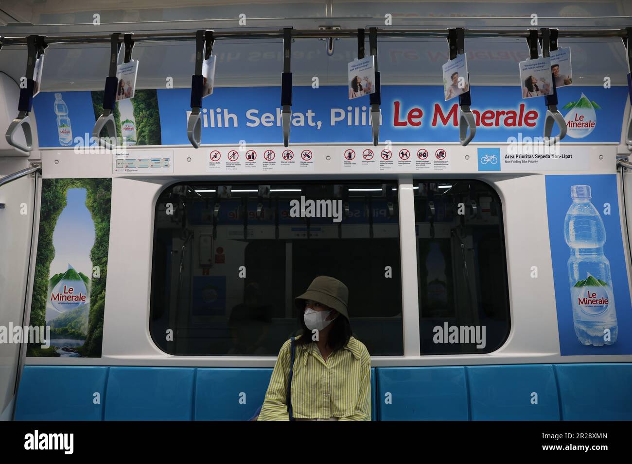 Jeune indonésienne portant un masque dans un wagon vide de Mass Rapid Transit avec la publicité le Minerale affichée au-dessus de sa tête à Jakarta, Indonésie Banque D'Images