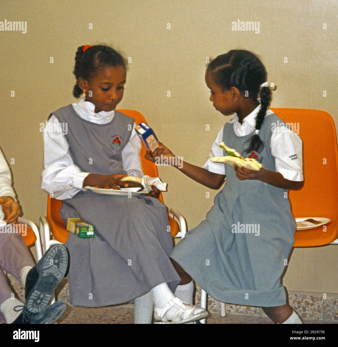 Abu Dhabi UAE Kindergarten School Birthday Party enfants manger nourriture fille passage jus carton à un ami Banque D'Images