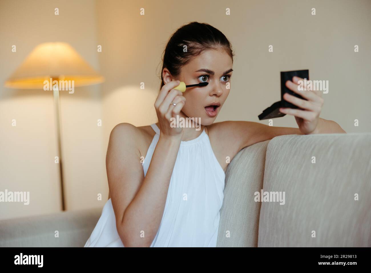 Une femme à la maison regarde dans le miroir et d'appliquer le maquillage colorant mascara cils, concept de beauté, le soin de la peau de problème avec l'acné. Photo de haute qualité Banque D'Images