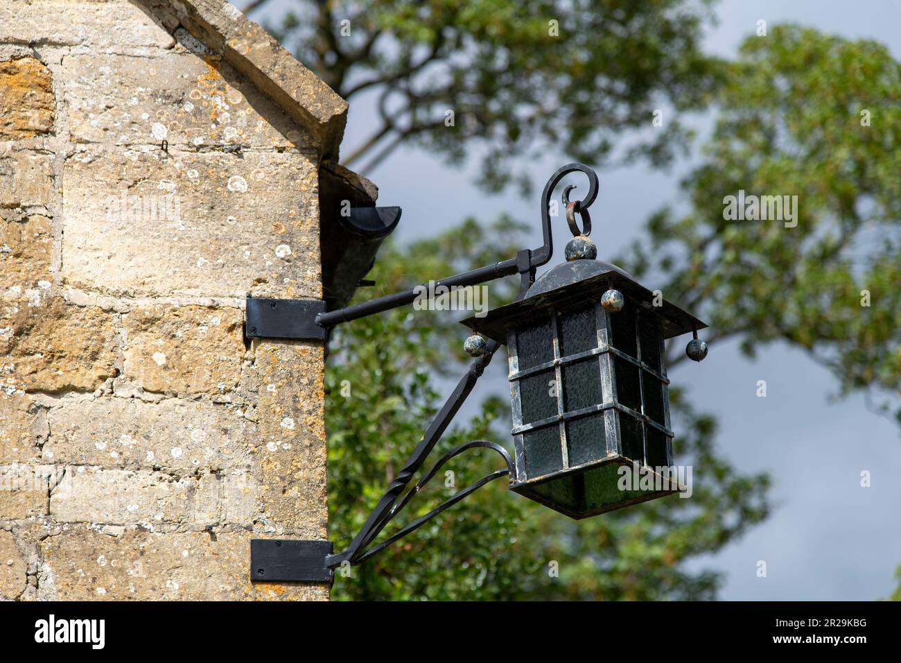 Vue rapprochée à angle bas d'une lanterne extérieure traditionnelle sur le côté d'un cottage typique des Cotswolds, au Royaume-Uni, en pierre calcaire avec ciel et arbres hors du foyer Banque D'Images