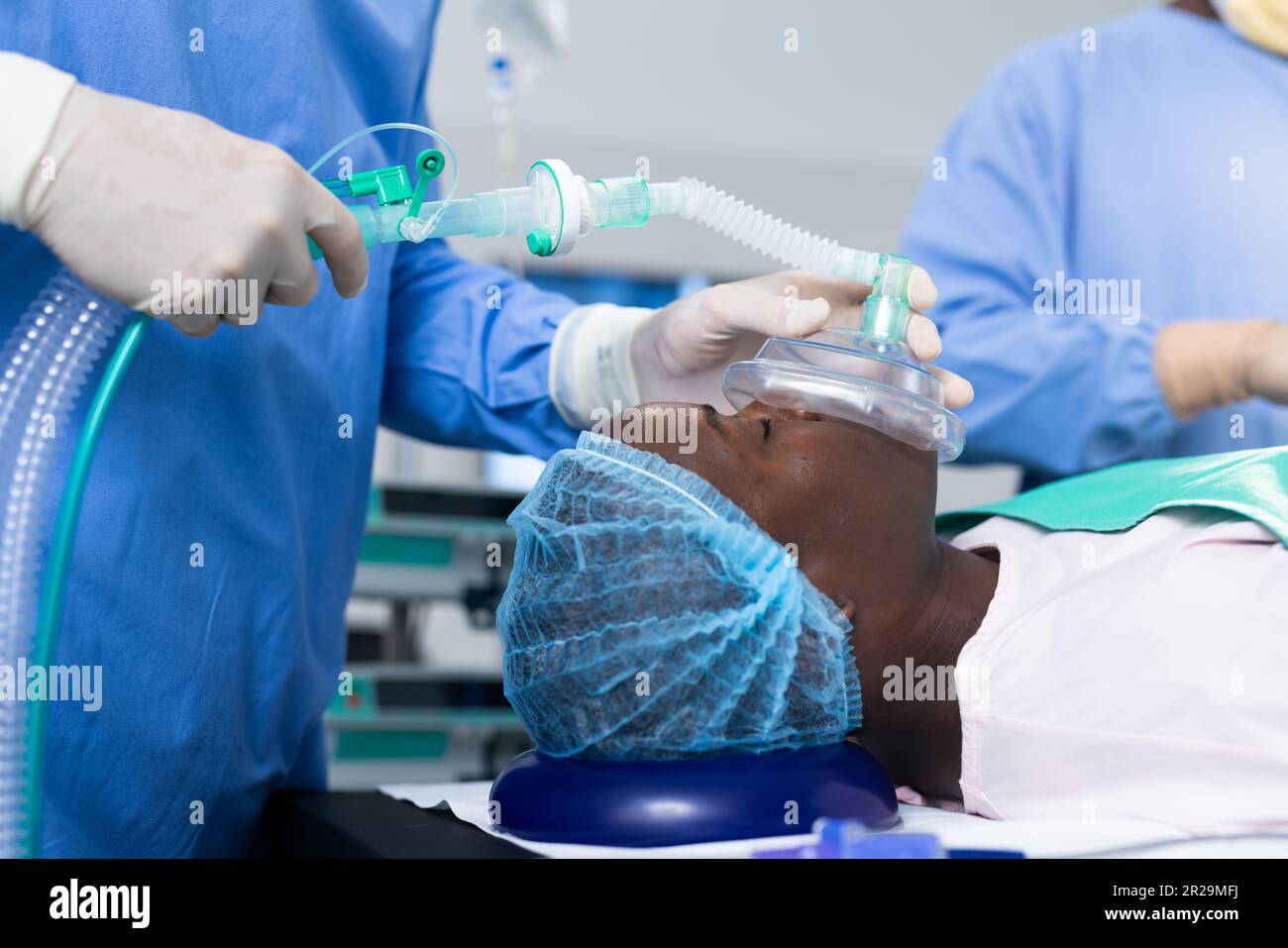 Section médiane du chirurgien donnant un masque anesthésique de patient mâle afro-américain dans le bloc opératoire Banque D'Images