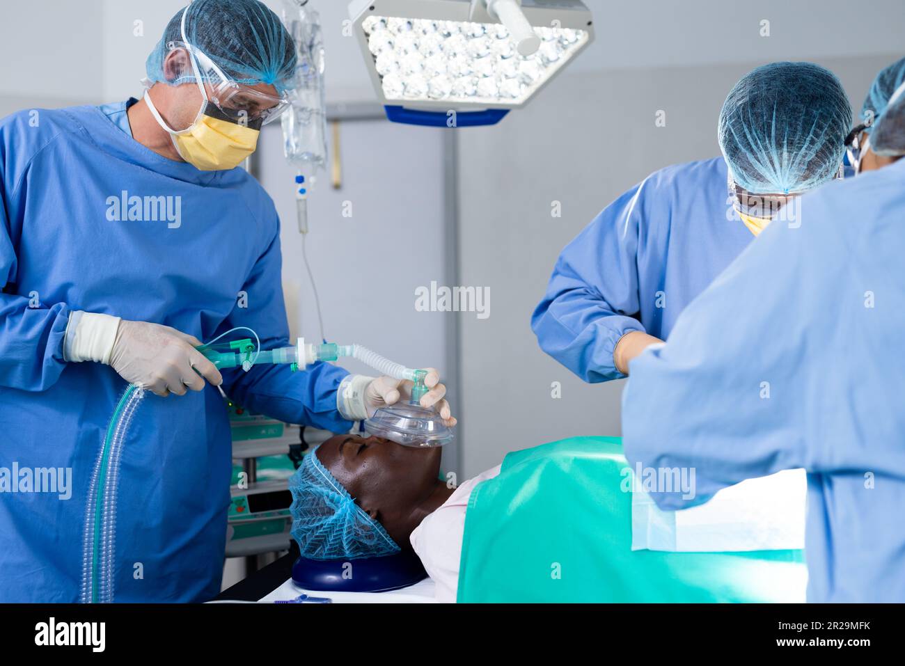 Divers groupes de chirurgiens dont le patient est masculin reçoivent un masque anesthésique dans le bloc opératoire Banque D'Images