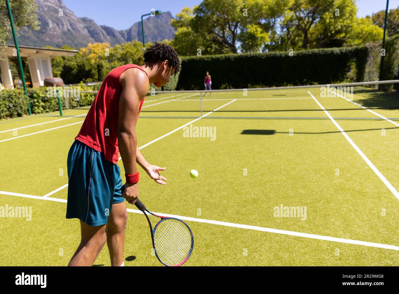 Homme biracial avec raquette rebondissant balle pour servir au joueur sur le court de tennis extérieur ensoleillé, espace copie Banque D'Images