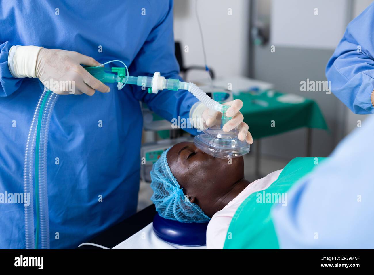 Section médiane du chirurgien donnant un masque anesthésique de patient mâle afro-américain dans le bloc opératoire Banque D'Images