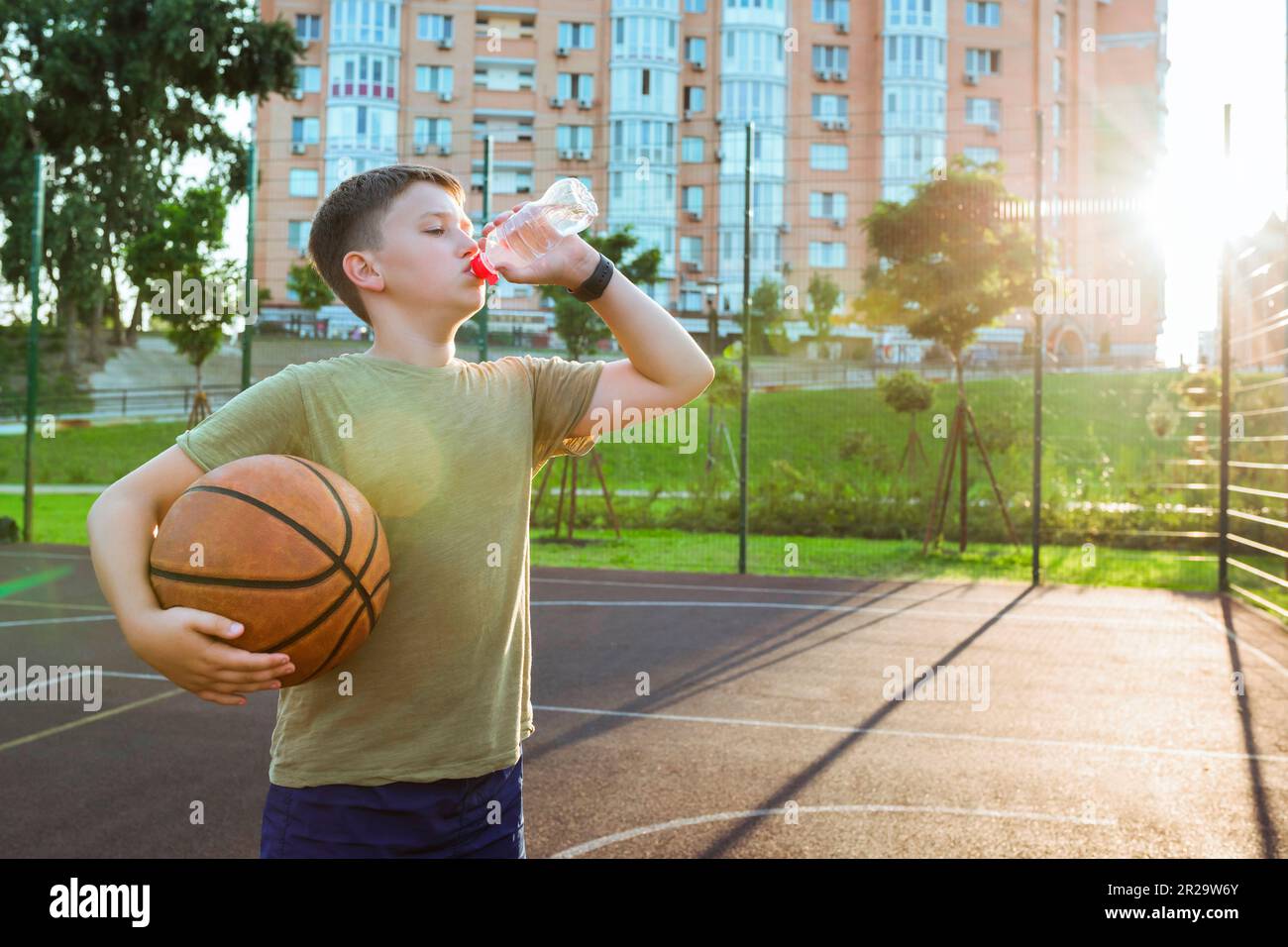 Un adolescent boit de l'eau sur une aire de jeux ouverte avec un ballon ...